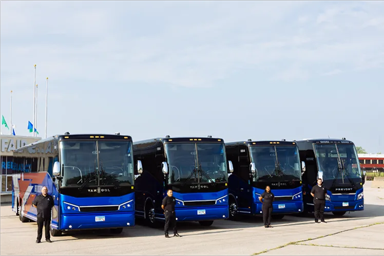 Four Lorenz Bus Service drivers in uniform standing in front of a lineup of Van Hool and Prevost motorcoaches