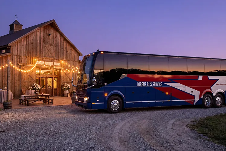 Lorenz Bus Service charter coach parked outside a warmly lit barn venue at dusk, ready for a wedding event