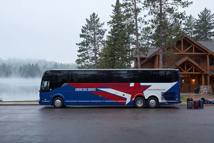 Lorenz Bus Service motorcoach parked outside a lakeside lodge on a misty morning, luggage staged beside the bus